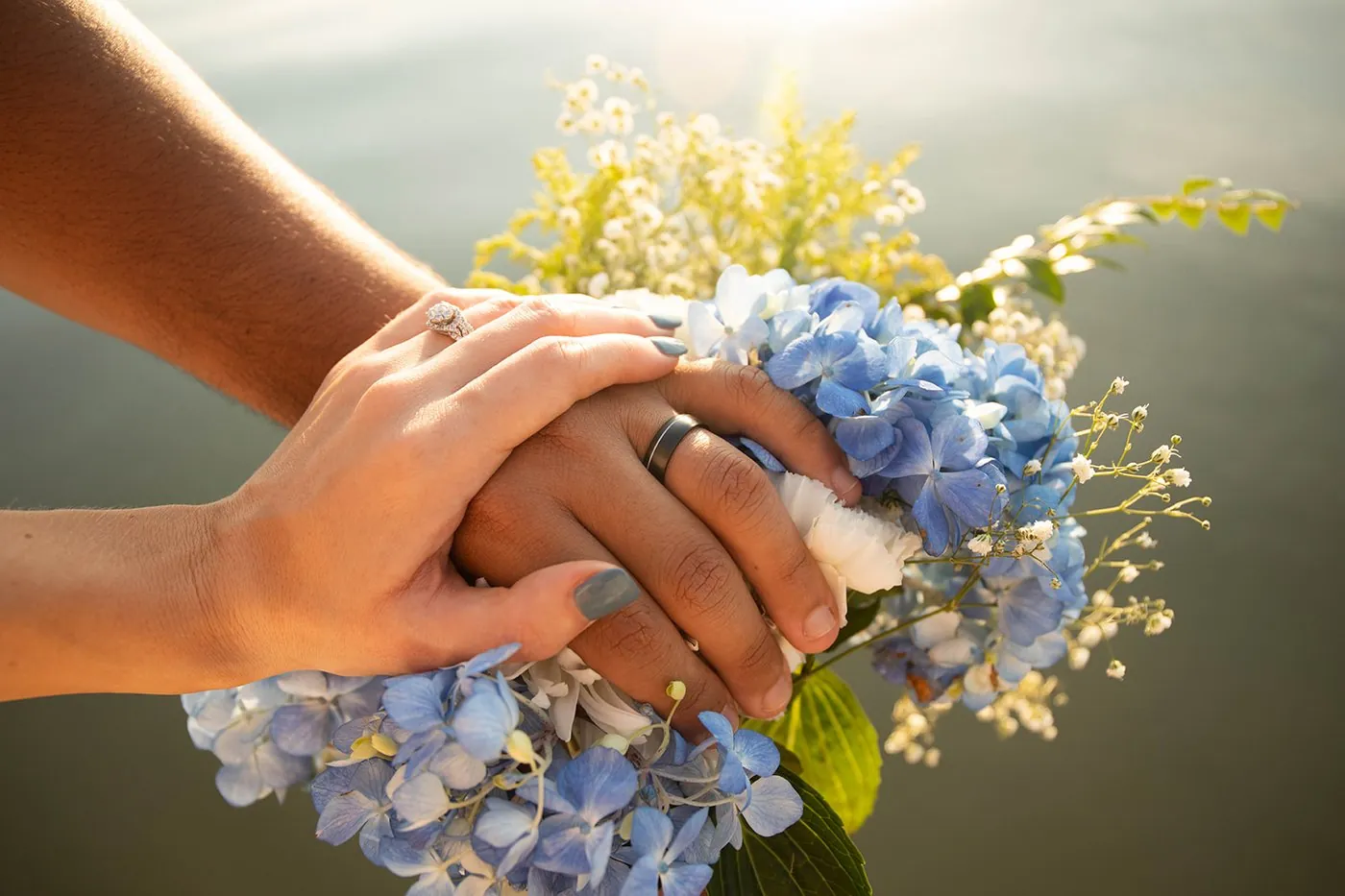 The couple's hands with their wedding rings resting on a blue hydrangea bouquet