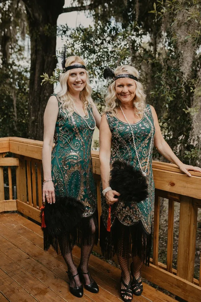 Two flapper bridesmaids in green and gold fringe dresses with feather fans