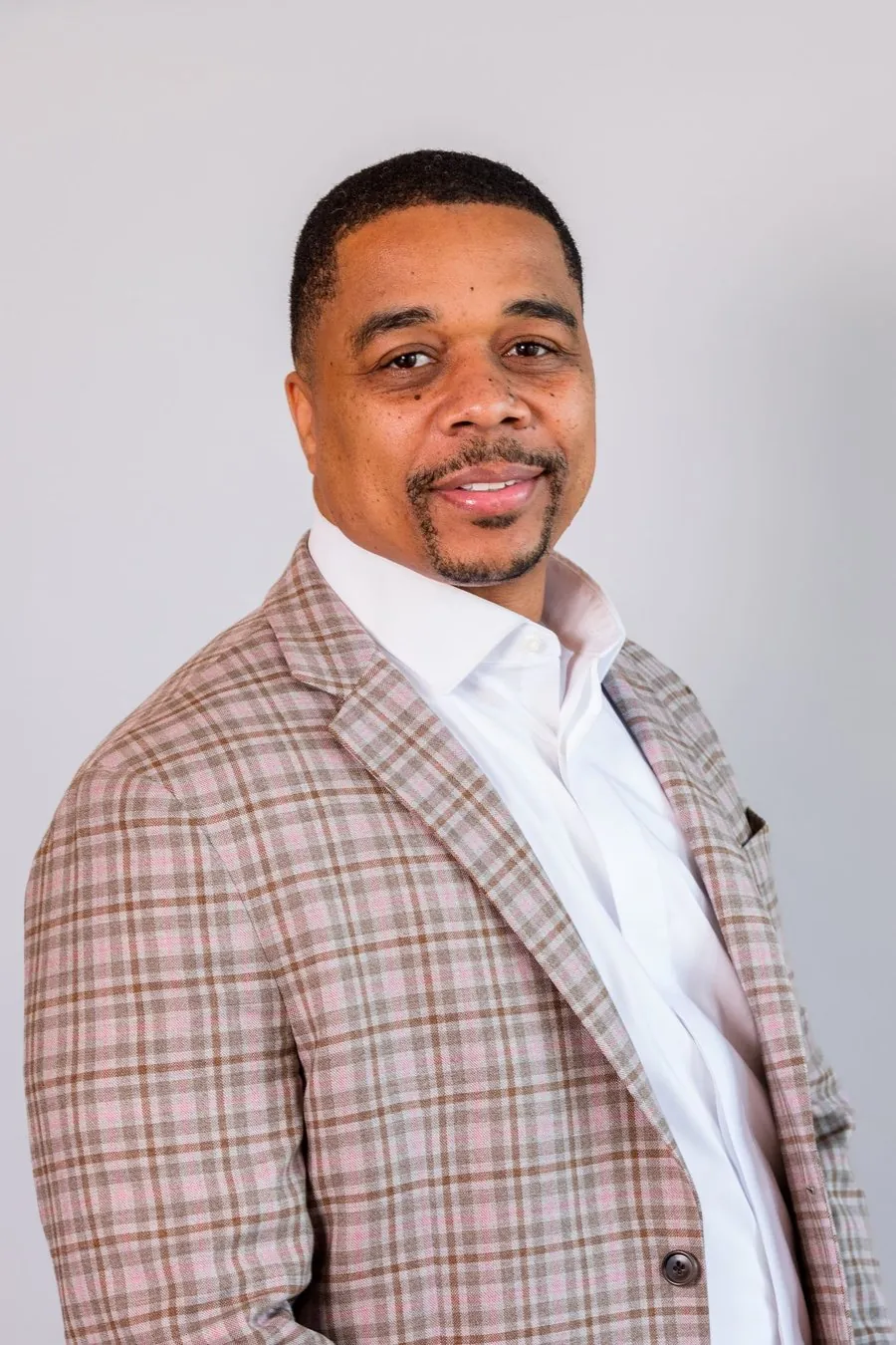A professional studio headshot of a businessman in a plaid blazer