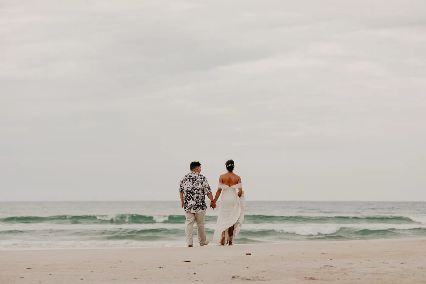 Destination wedding couple walking hand in hand toward the sea, photographed by Ohlson Photography