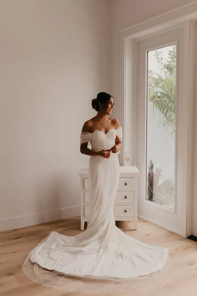 Camila lista para su boda, con vestido de encaje junto a la ventana