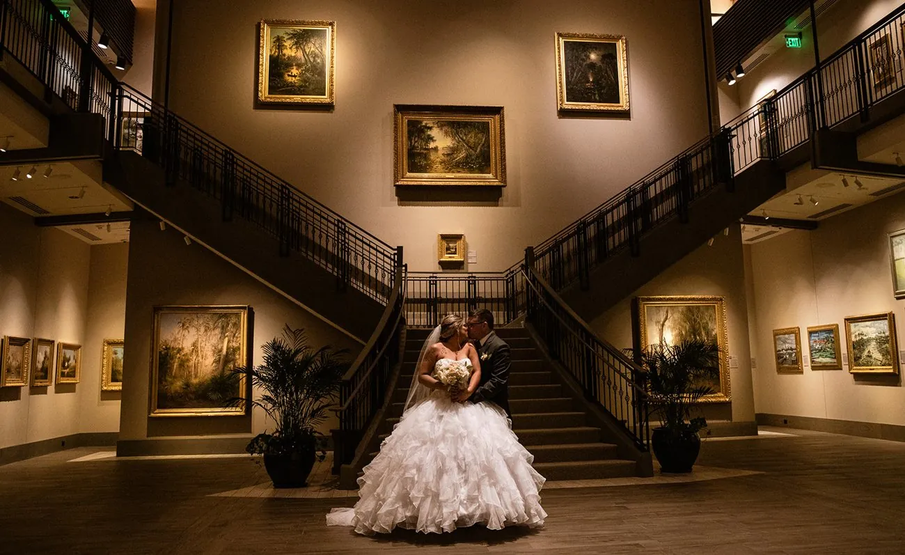 Haley and Matt embracing in the grand two-story gallery beneath the Florida art collection