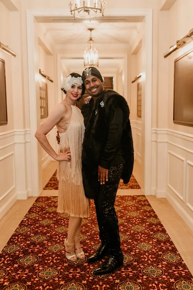 A glamorous couple in a fur stole and beaded 1920s attire in the ballroom hallway