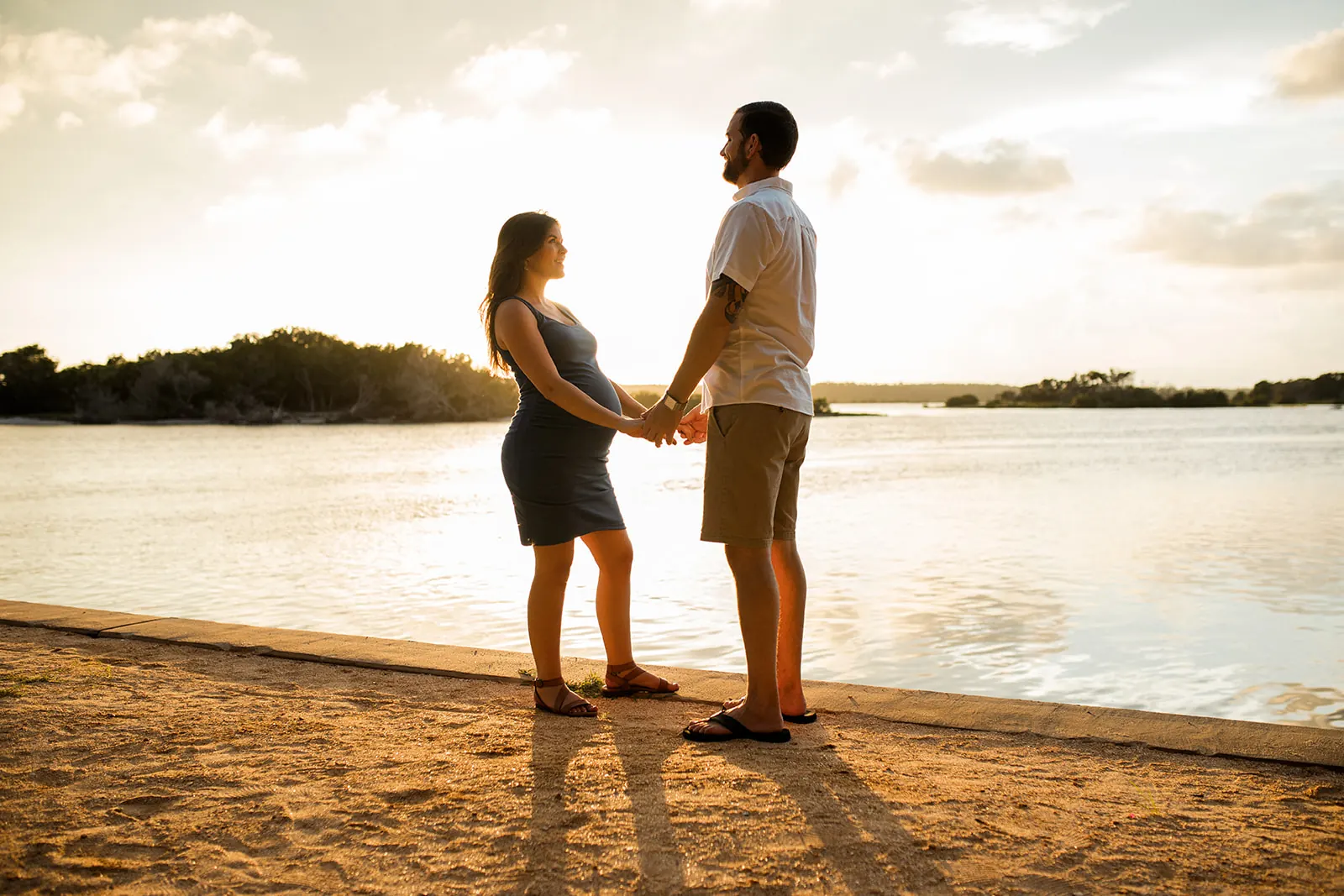 Christine and Jordan holding hands at golden sunset over the water during their Washington Oaks maternity session