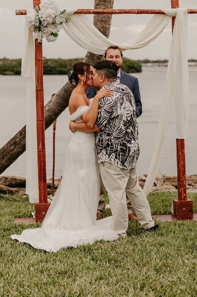 Marty y Camila en su primer beso bajo un arco de bambú junto al agua