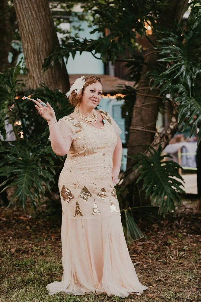 A 1920s bride in a champagne beaded flapper gown with a feather headpiece and cigarette holder