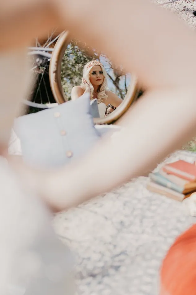 An Alice in Wonderland bride reflected in a round looking-glass among books