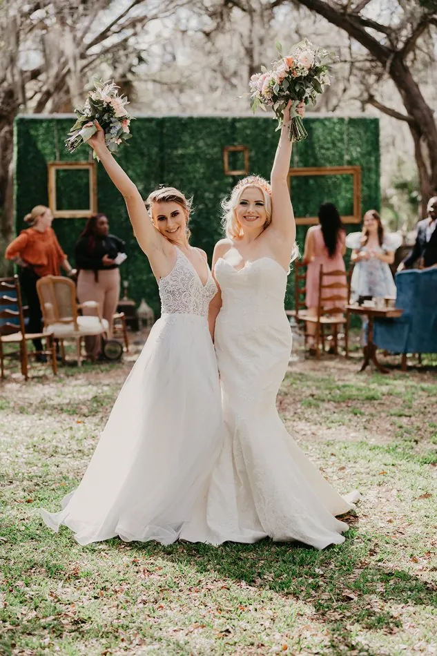 Two brides raising their bouquets in celebration