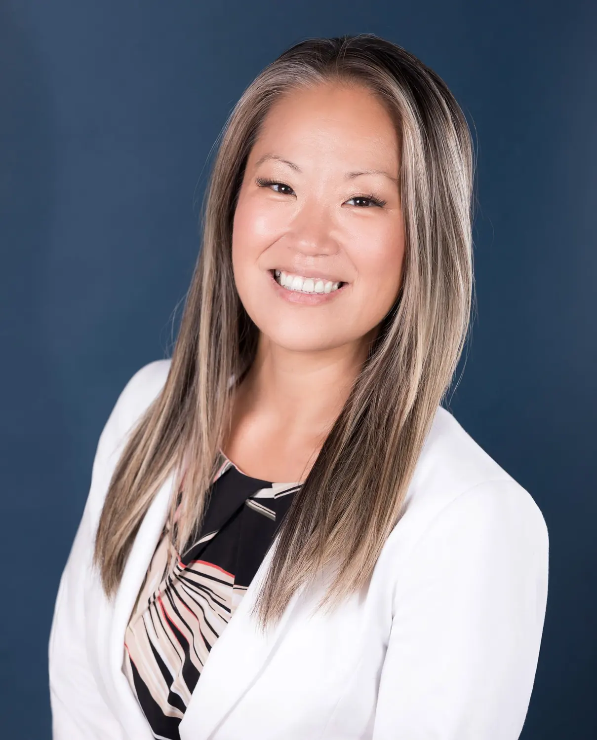 Professional headshot of a businesswoman in a white blazer on a navy studio backdrop