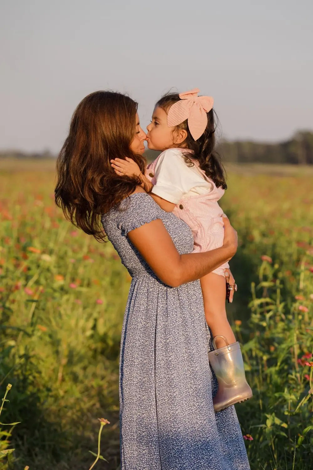 Paola kissing her daughter Lily in a flower field at sunset