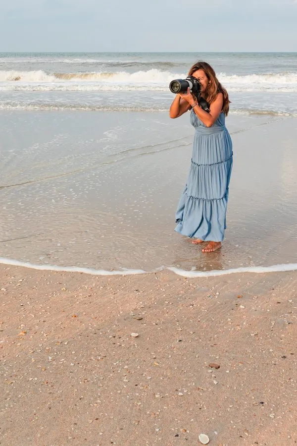 Paola photographing barefoot at the water's edge in a blue dress