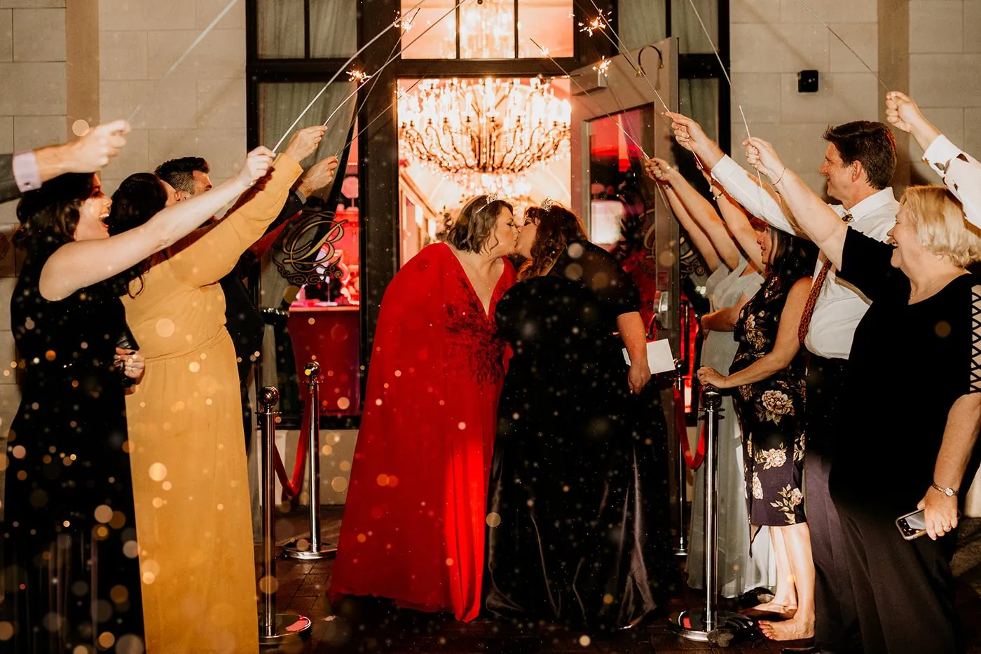 The two brides kissing during a sparkler send off as guests cheer