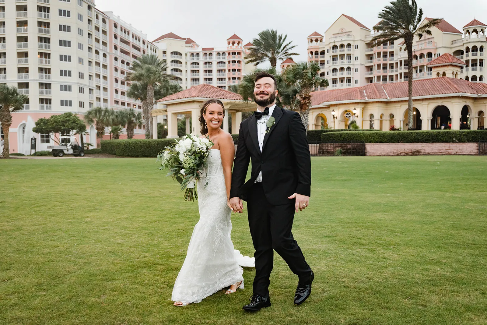 A bride and groom walking hand in hand on the lawn at Hammock Beach Resort on Florida's Historic Coast