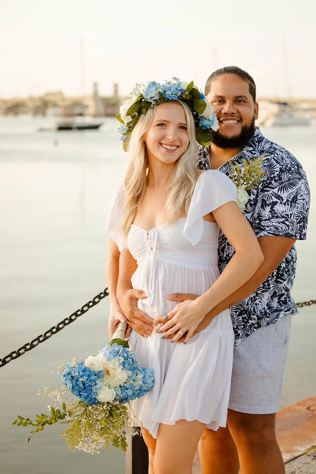 A bride in a flower crown and her groom holding a hydrangea bouquet by the water