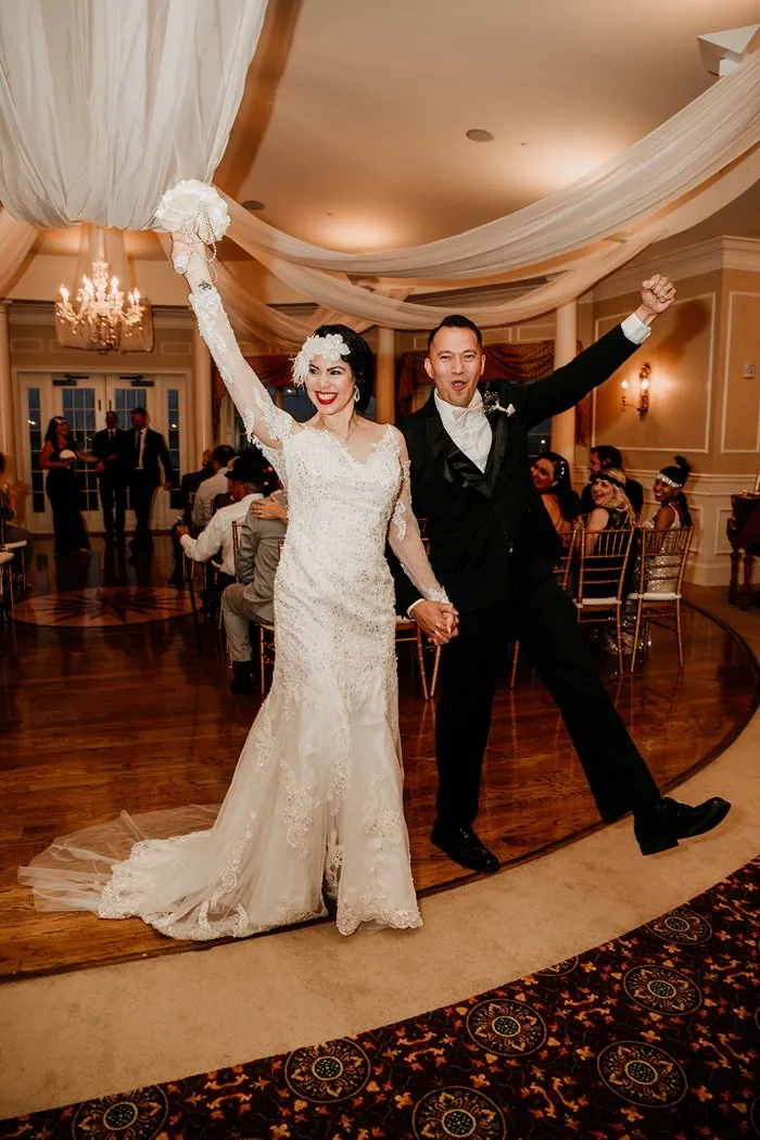 Rita and Eddie entering their 1920s Great Gatsby wedding reception, arms raised in celebration