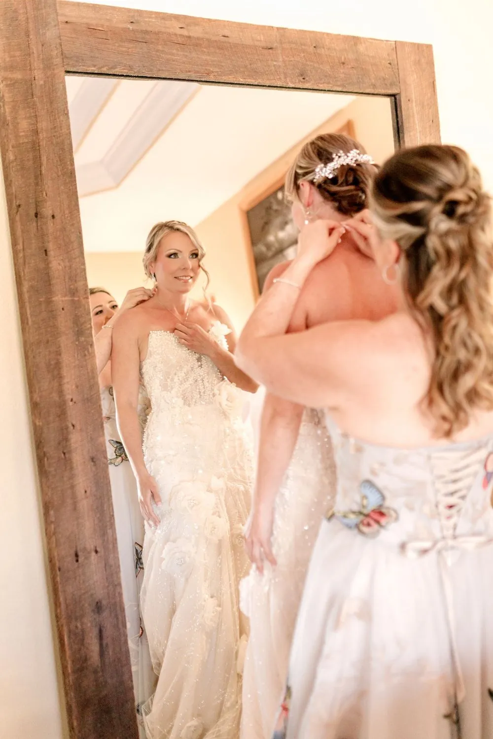 Bride having her earrings fastened in the mirror before a small backyard wedding