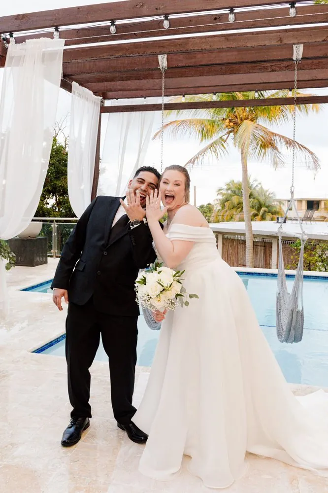 Victoria and Jose showing their wedding rings, laughing poolside at their Puerto Rico wedding