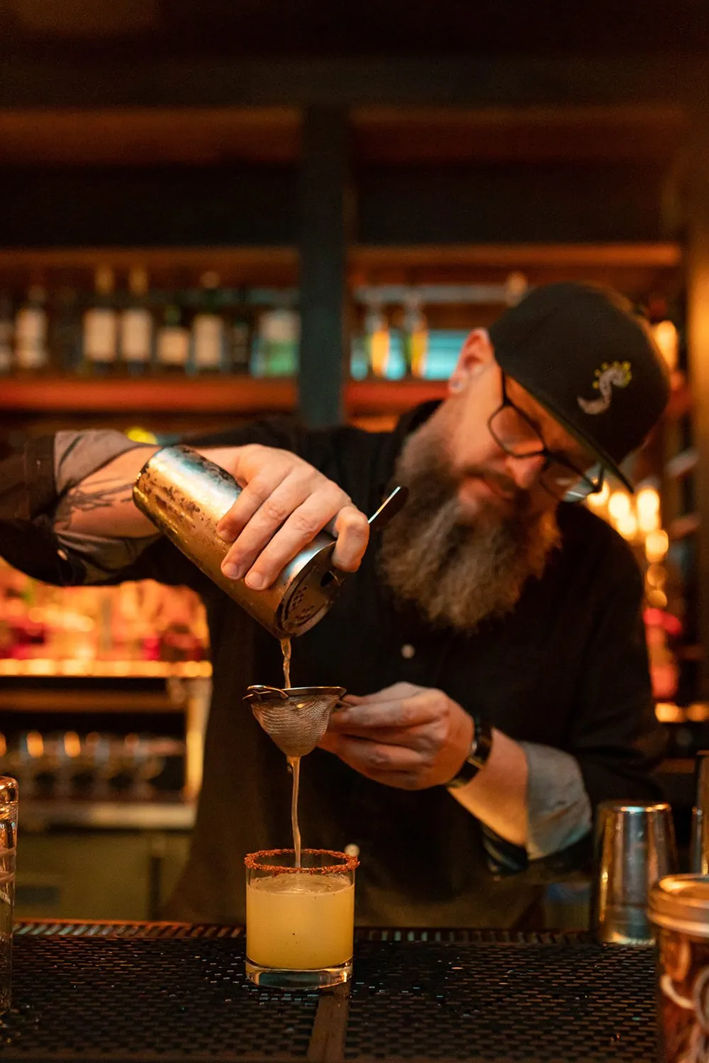 A bartender straining a craft cocktail at a moody bar