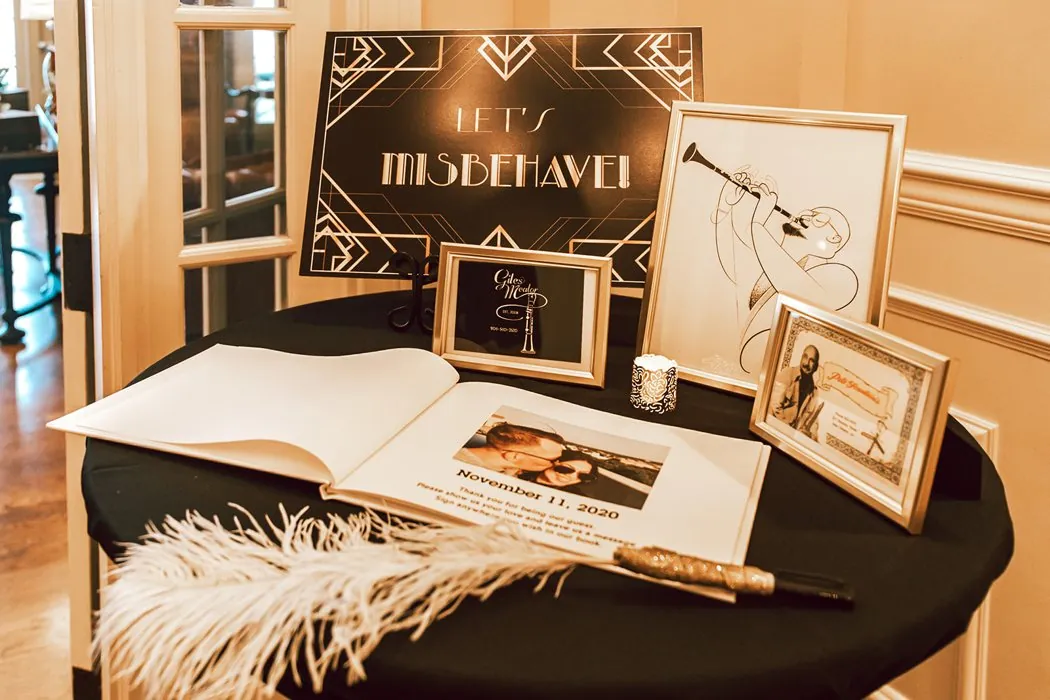 An art-deco Lets Misbehave sign and feathered guest book