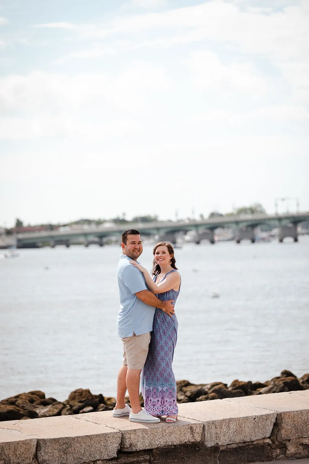 Katie and Daniel embracing on the St. Augustine seawall with the Bridge of Lions behind them