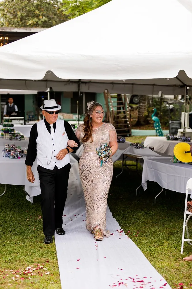 The bride walking the aisle with her father, both in 1920s attire