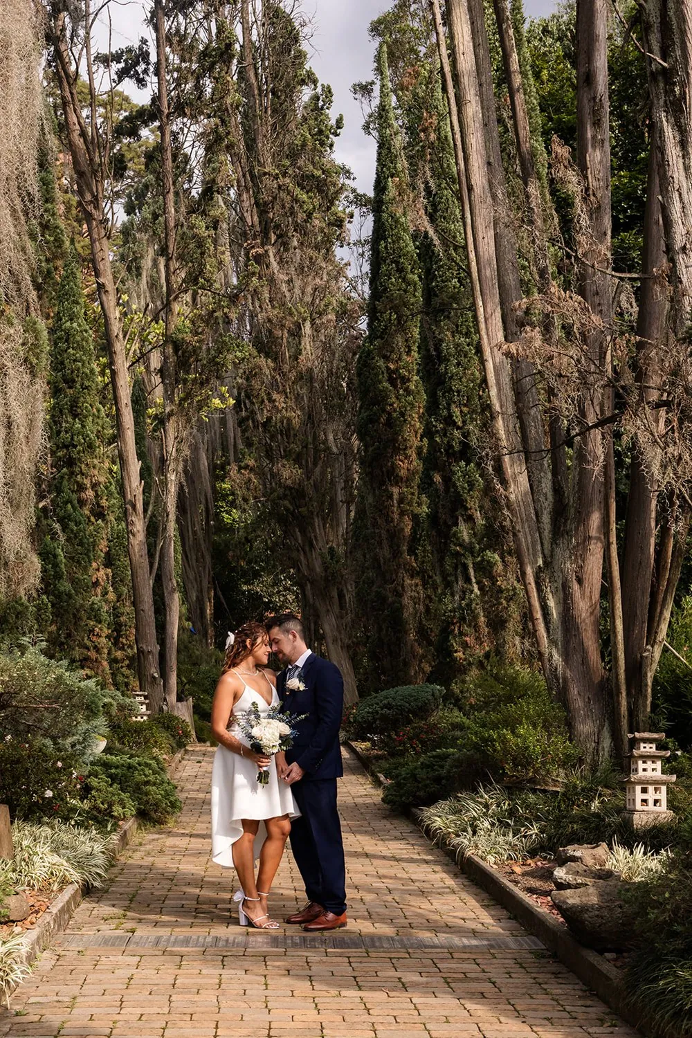 Nataly and Joey forehead to forehead on a cypress-lined garden path at El Castillo, Medellin, Colombia