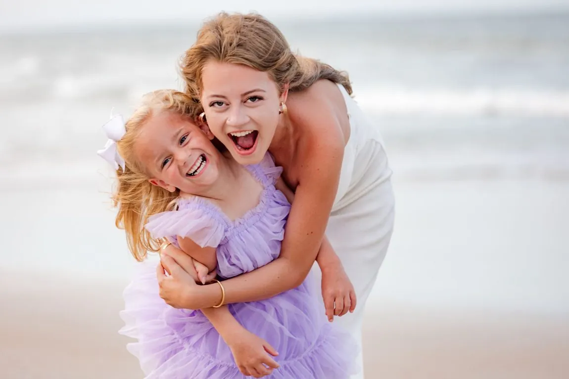 A big sister and little sister laughing and hugging on the beach