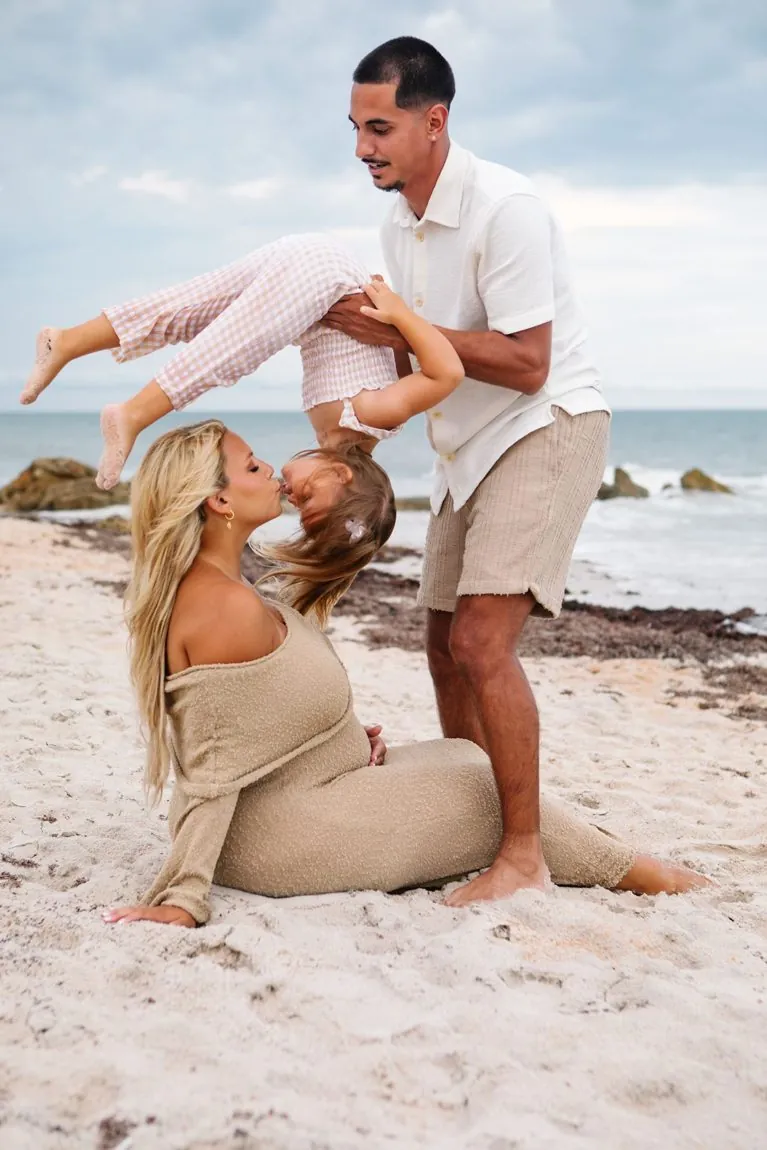 A family on the beach, dad lifting one child while mom kisses the other